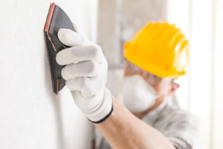 Sanding repaired wall surfaces to ensure an even finish before spraying paint